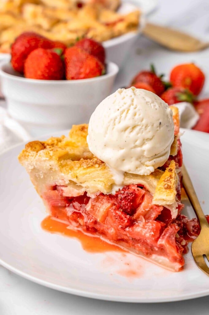 A slice of strawberry rhubarb pie with a scoop of ice cream on top