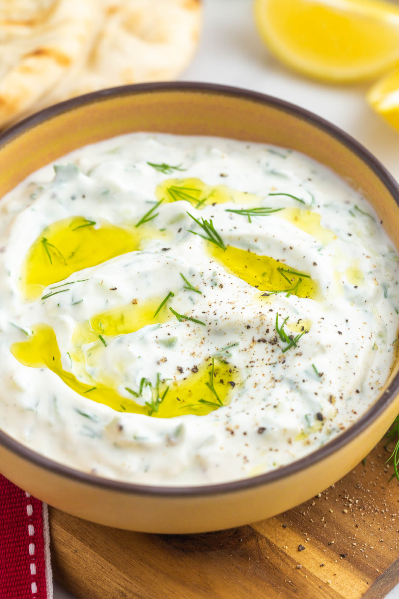 A bowl of creamy tzatziki dip, drizzled with olive oil and garnished with fresh dill.