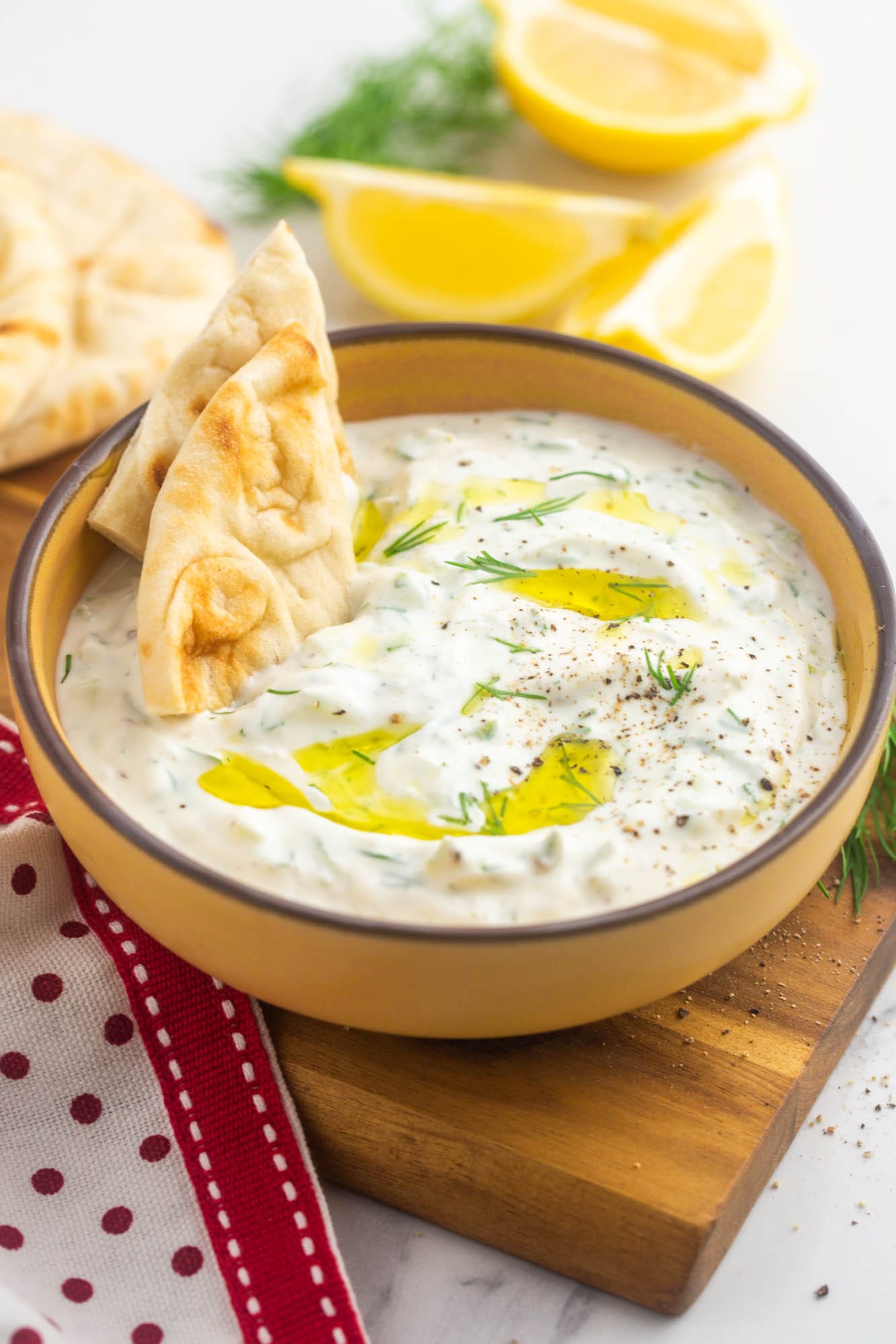A bowl of tzatziki topped with extra virgin olive oil, fresh herbs, and pita triangles.