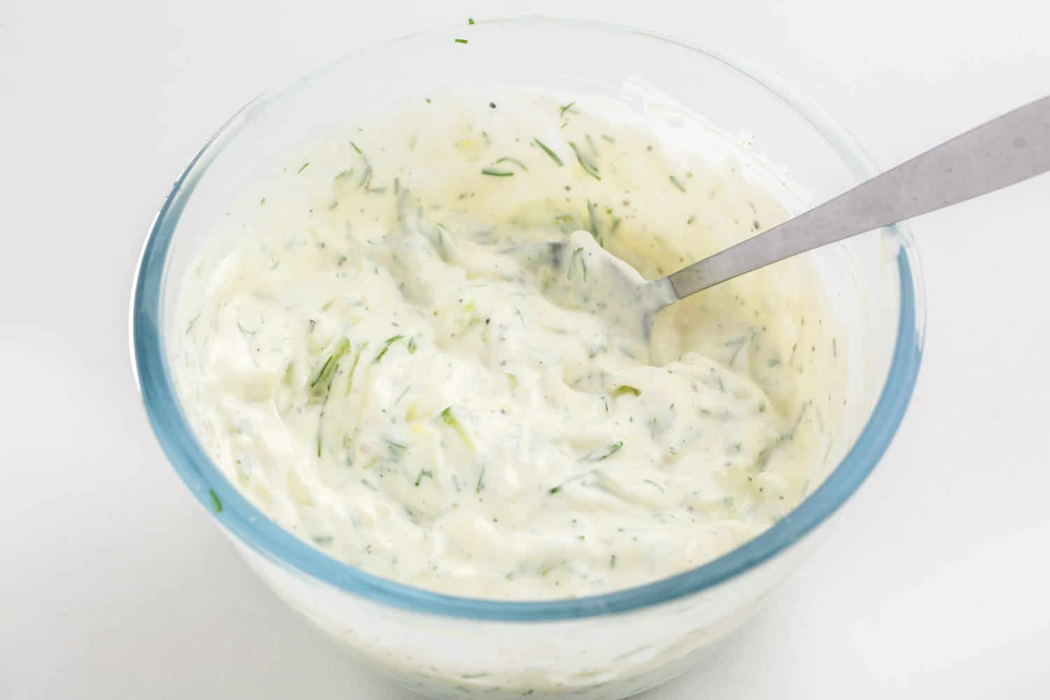 Mixed tzatziki sauce in a glass bowl with a spoon