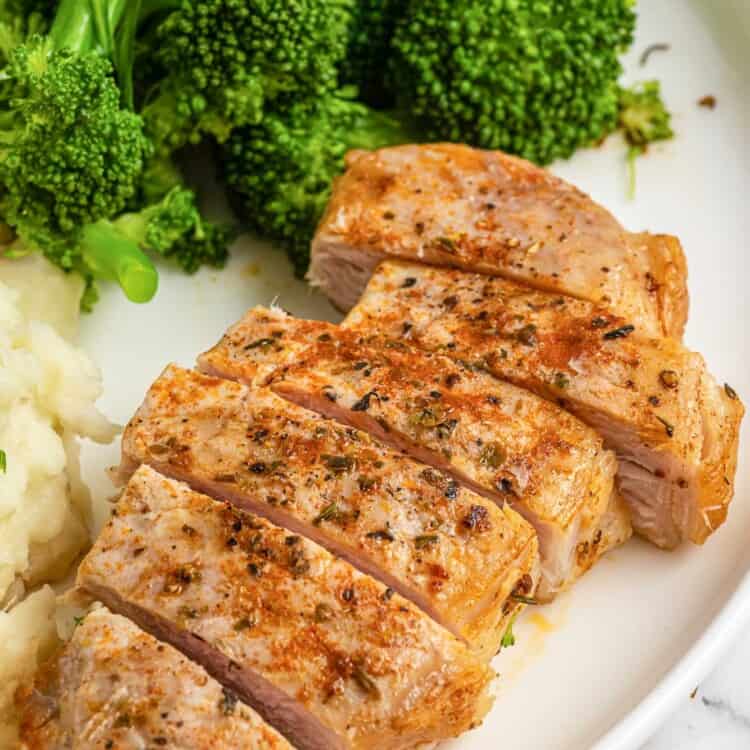 Sliced air fried pork chop on a white plate, served with mashed potatoes and steamed broccoli.