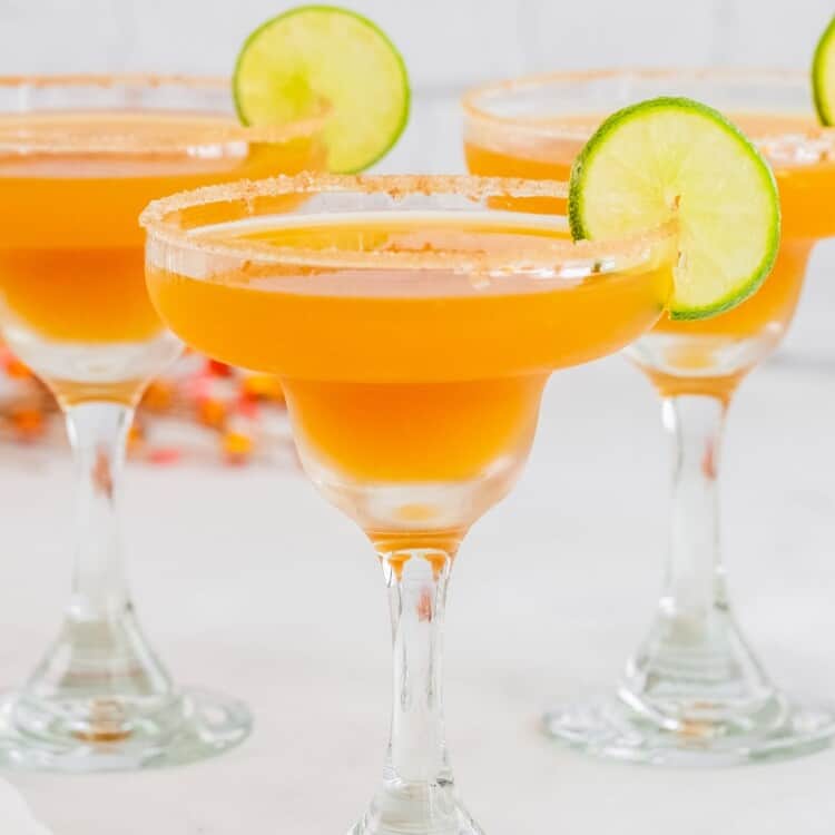 three apple cider margaritas with sugar rims and lime slices.