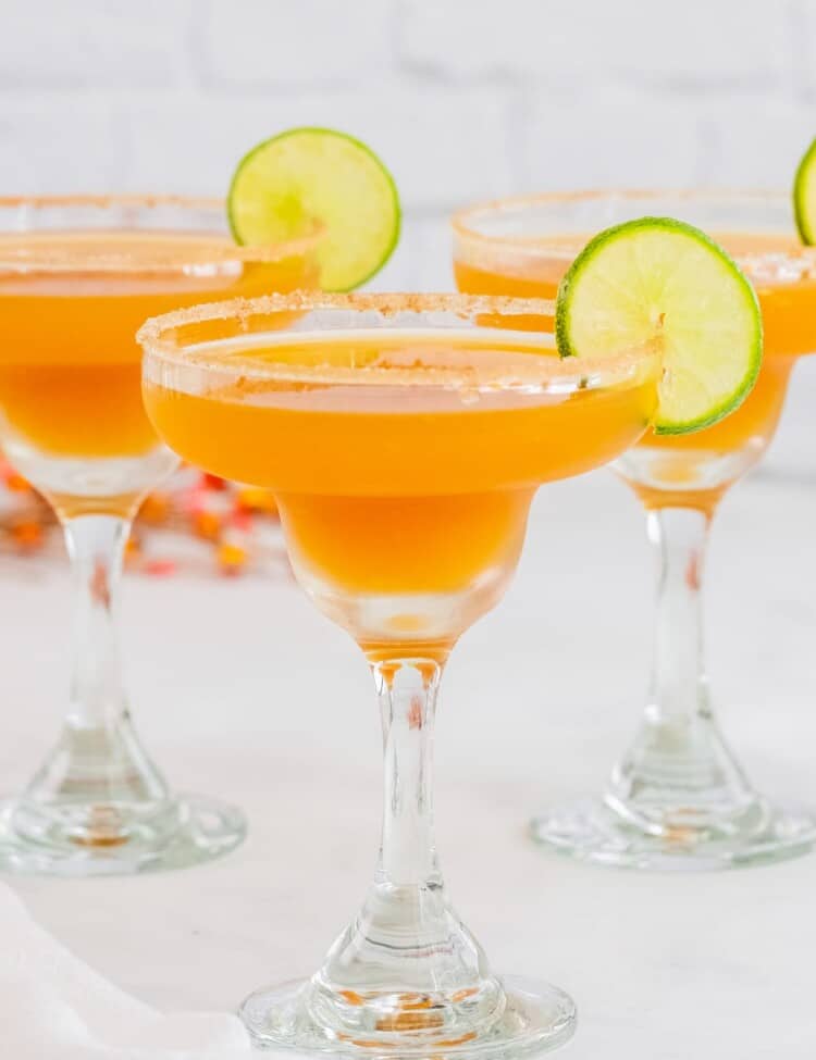 three apple cider margaritas with sugar rims and lime slices.