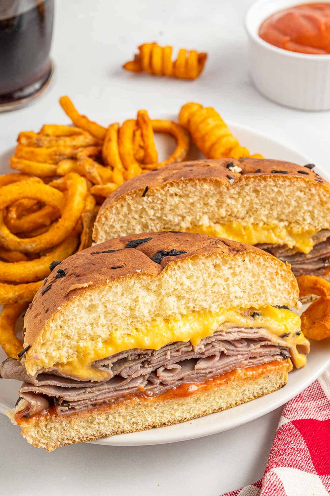a copycat arby's sandwich cut in half on a plate with curly fries