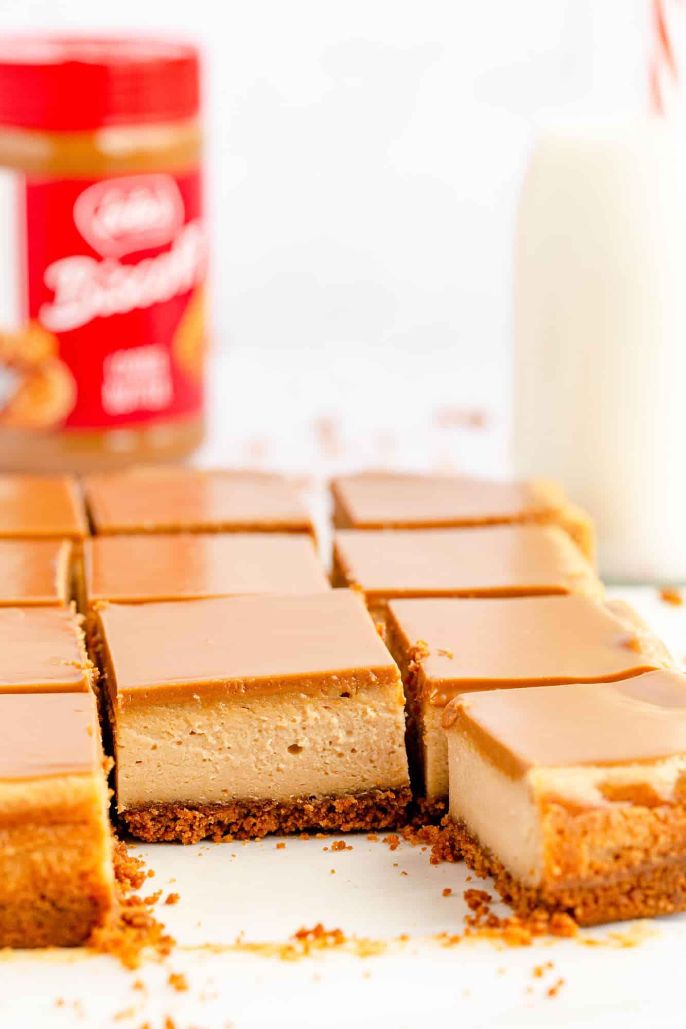 a batch of biscoff cheesecake bars lined up on the counter in front of a jar of lotus cookie butter