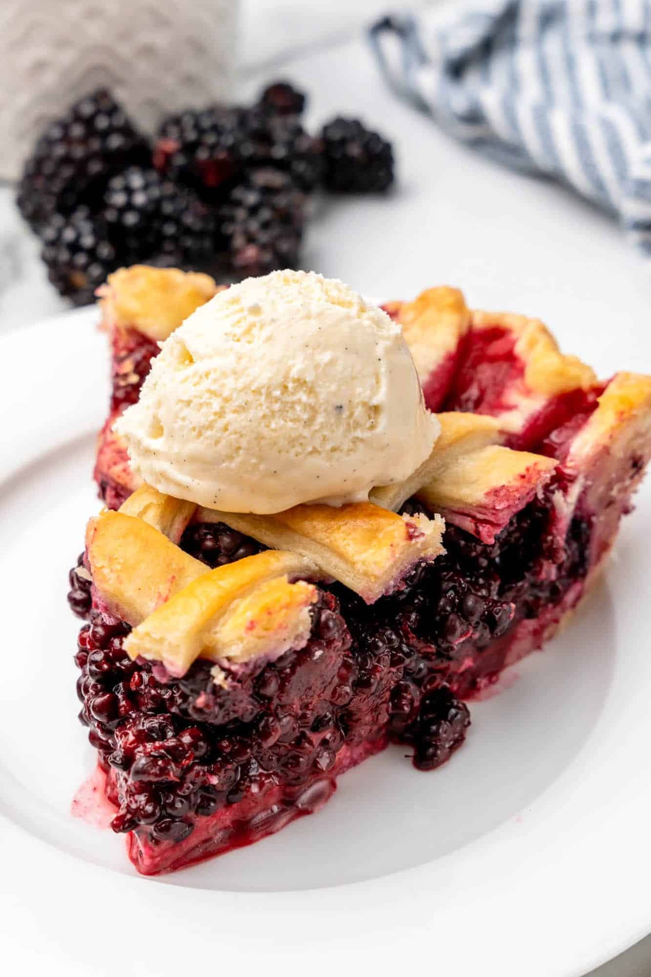 a slice of blackberry pie with lattice top, with a scoop of vanilla ice cream on top