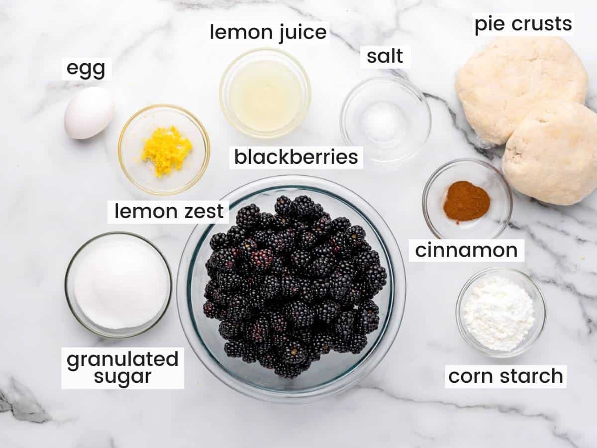 a bowl of fresh blackberries, surrounded by smaller bowls with all of the ingredients to make a pie