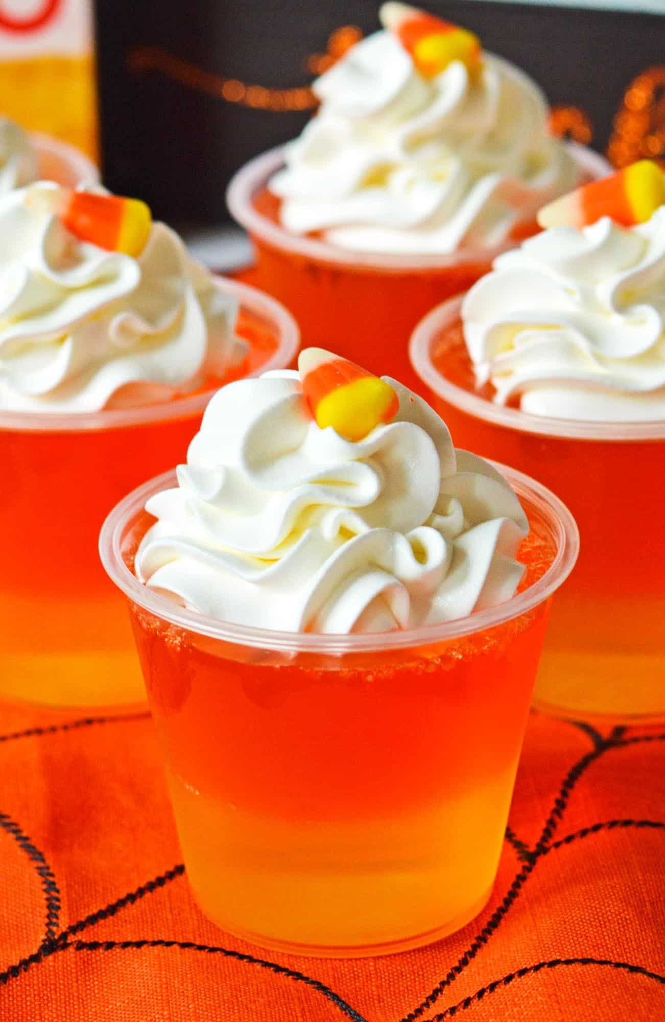 4 orange and yellow layered jello cups topped with whipped cream and candy corn. 