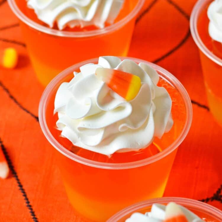 Candy corn Jello cups on a halloween tablecloth, viewed from above.