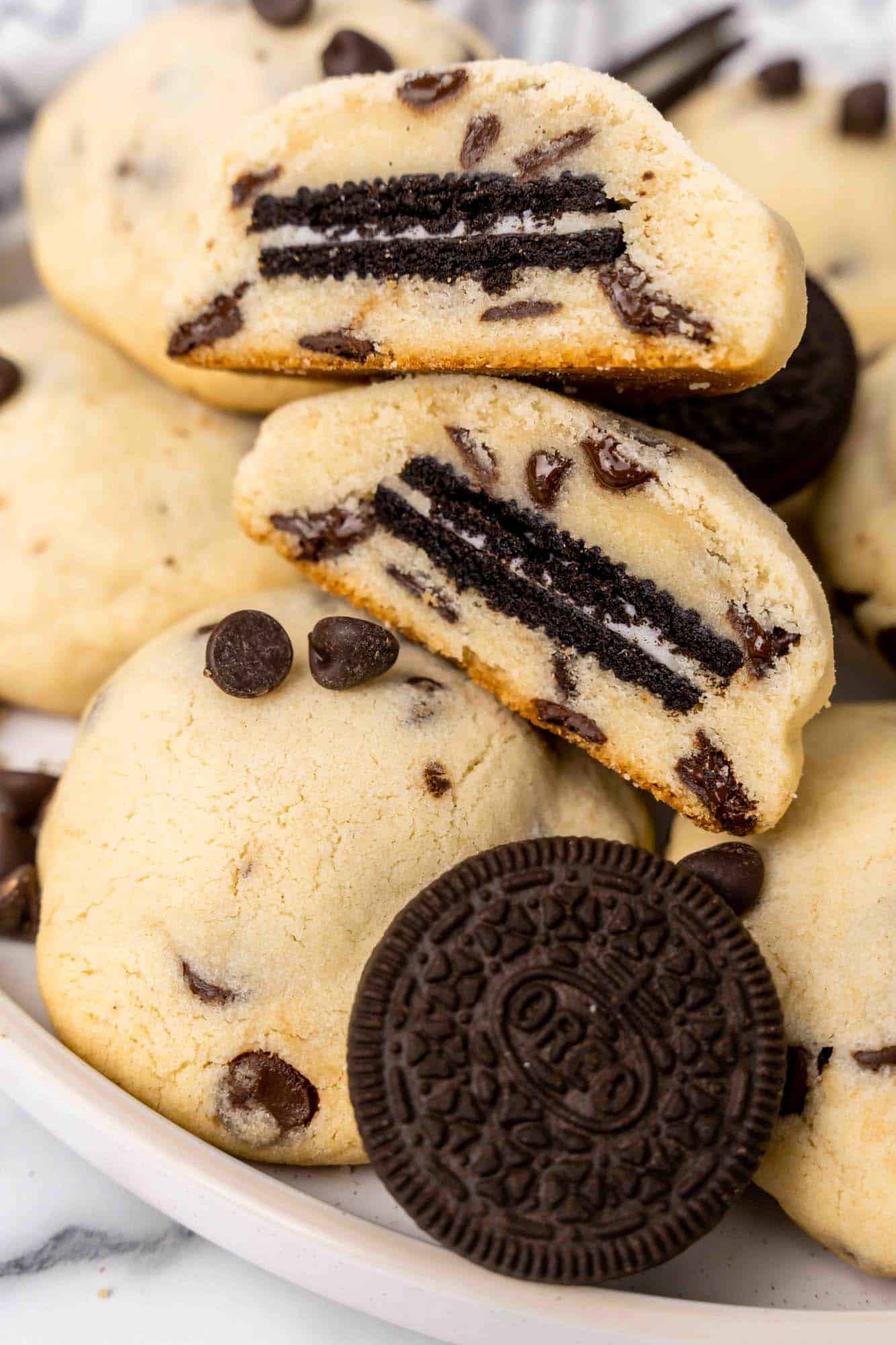 Thick chocolate chip cookies with Oreos inside. One is cut in half to show what it looks like in the middle. 