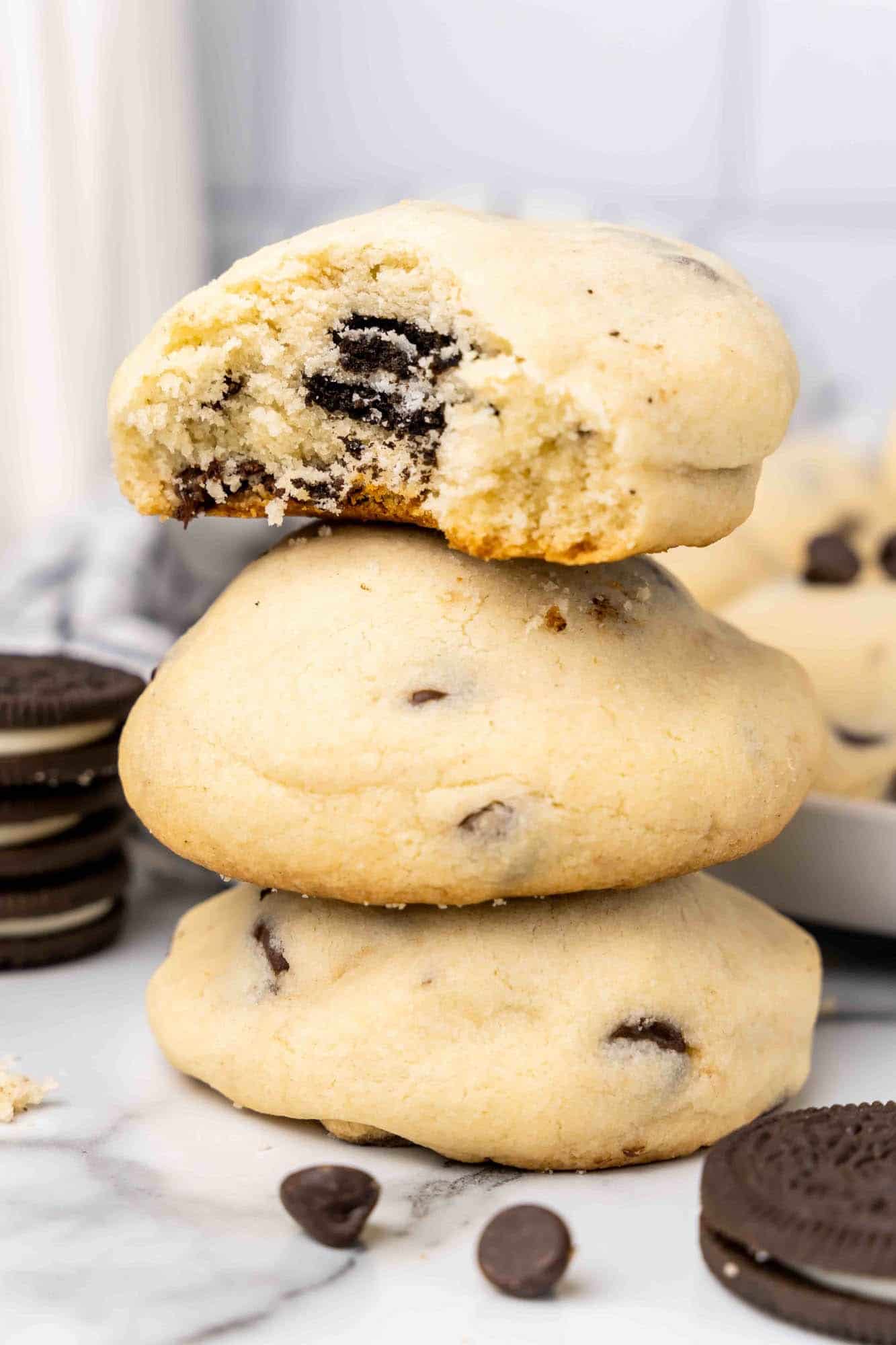 Three oreo stuffed chocolate chip cookies in a tall stack. The top one has a bite taken. 