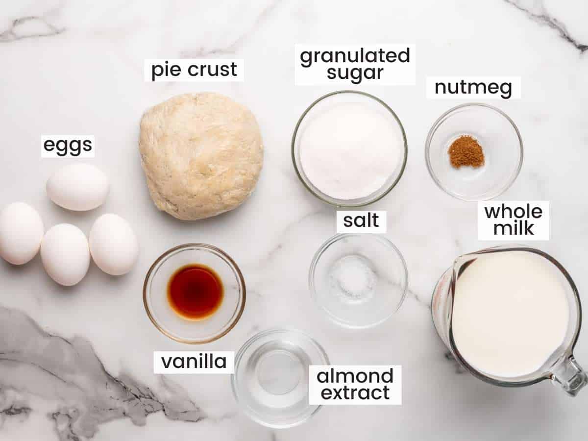 The ingredients for making a classic custard pie, all measured out and placed on a marble counter, viewed from above. 