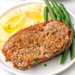 a slice of instant pot meatloaf on a white dinner plate with buttered potatoes and green beans.