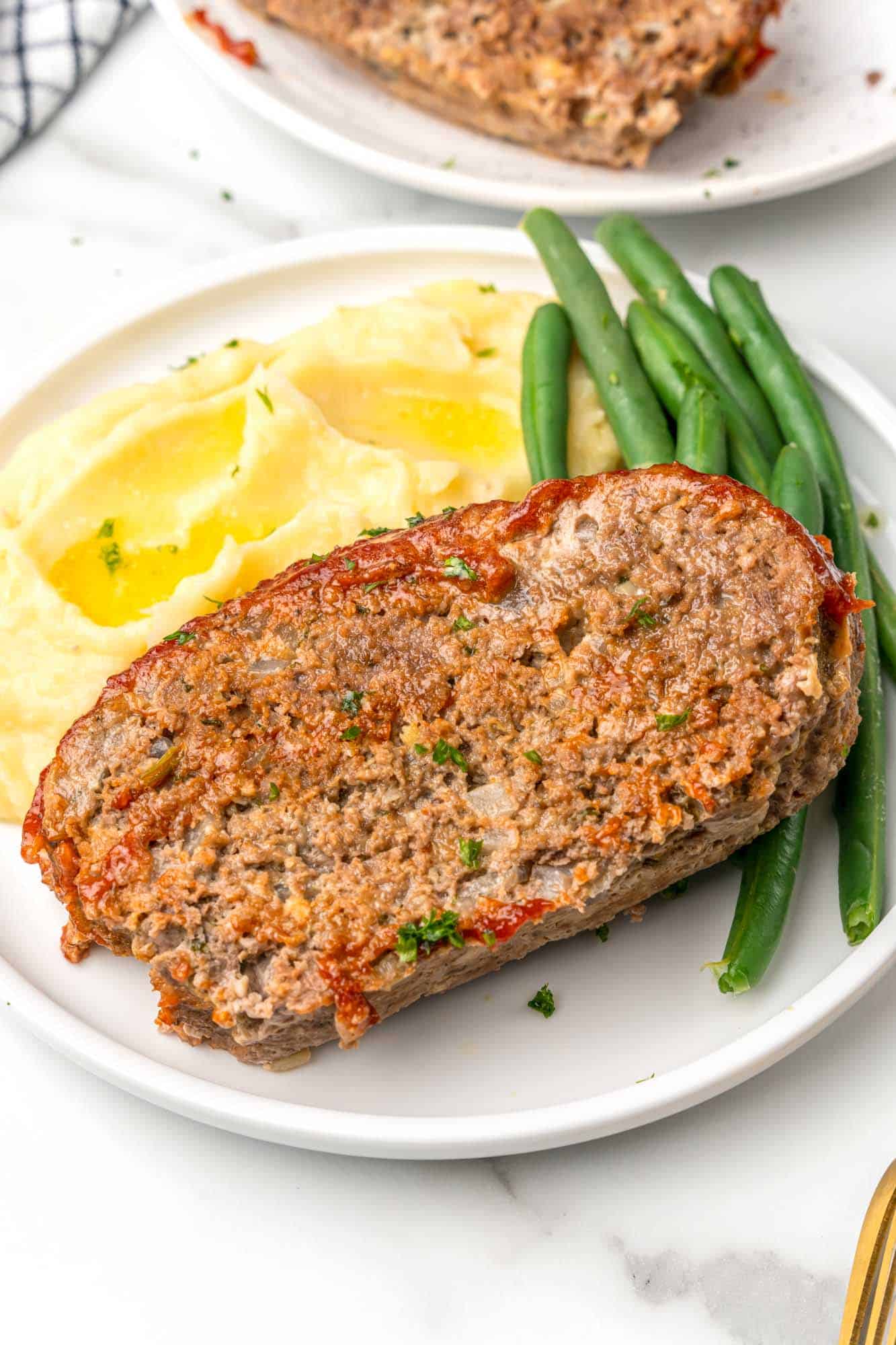 a slice of instant pot meatloaf on a white dinner plate with buttered potatoes and green beans.