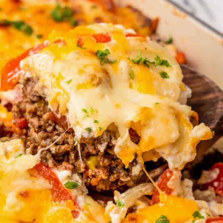 a square of layered john wayne casserole with ground beef and cheese, being lifted out of the dish with a spatula