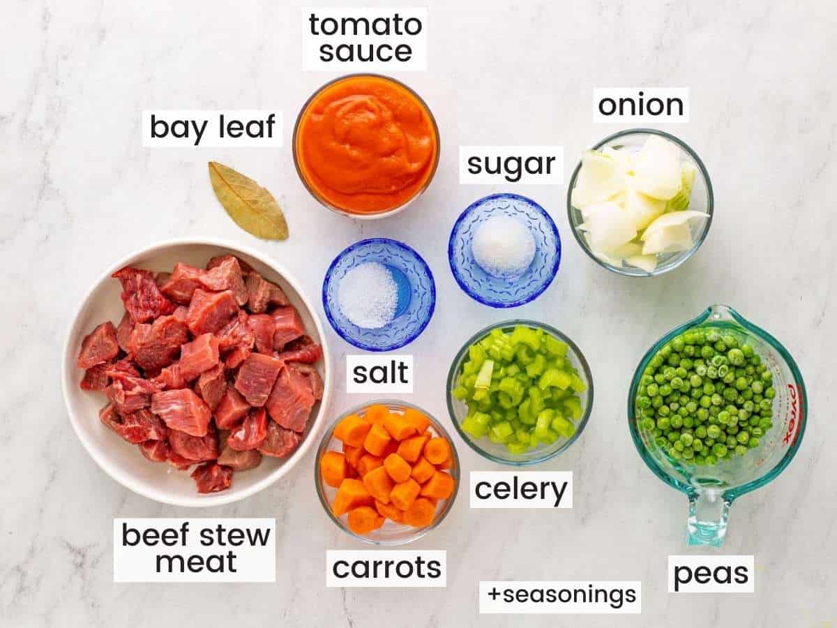 The ingredients needed to make beef stew, all in separate bowls on a marble countertop