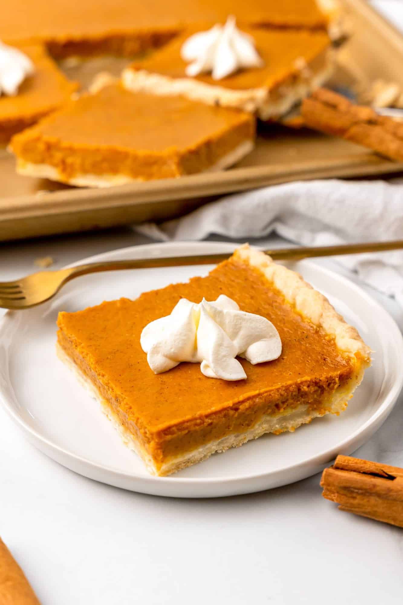 a square piece of pumpkin slab pie topped with whipped cream, on a white plate. 
