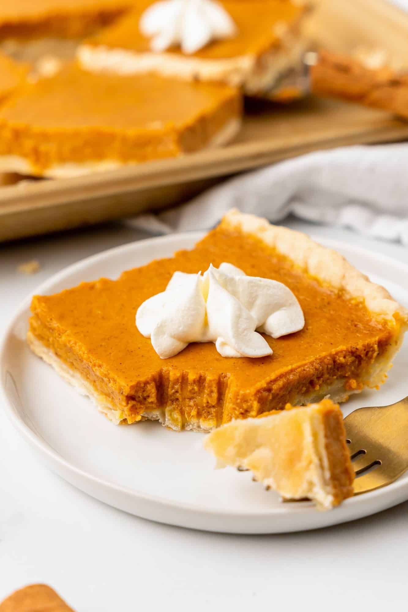a square piece of pumpkin slab pie on a plate with a bite taken out. 