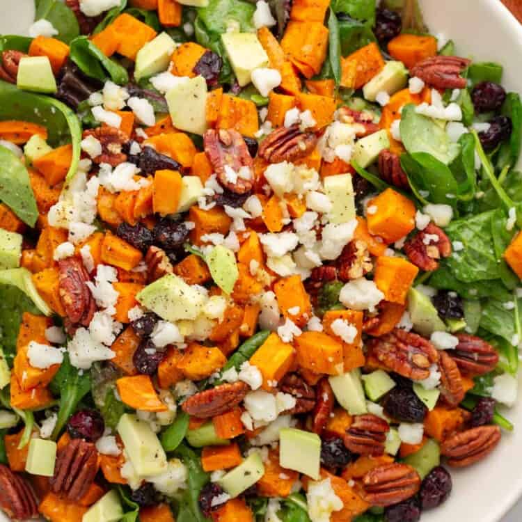 a large bowl filled with greens and a rustic roasted sweet potato salad.