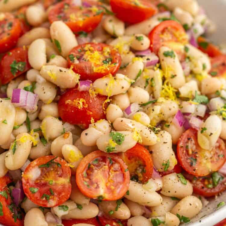 At an angle shot of white bean salad in a bowl, with cherry tomatoes, parsley, and lemon zest.