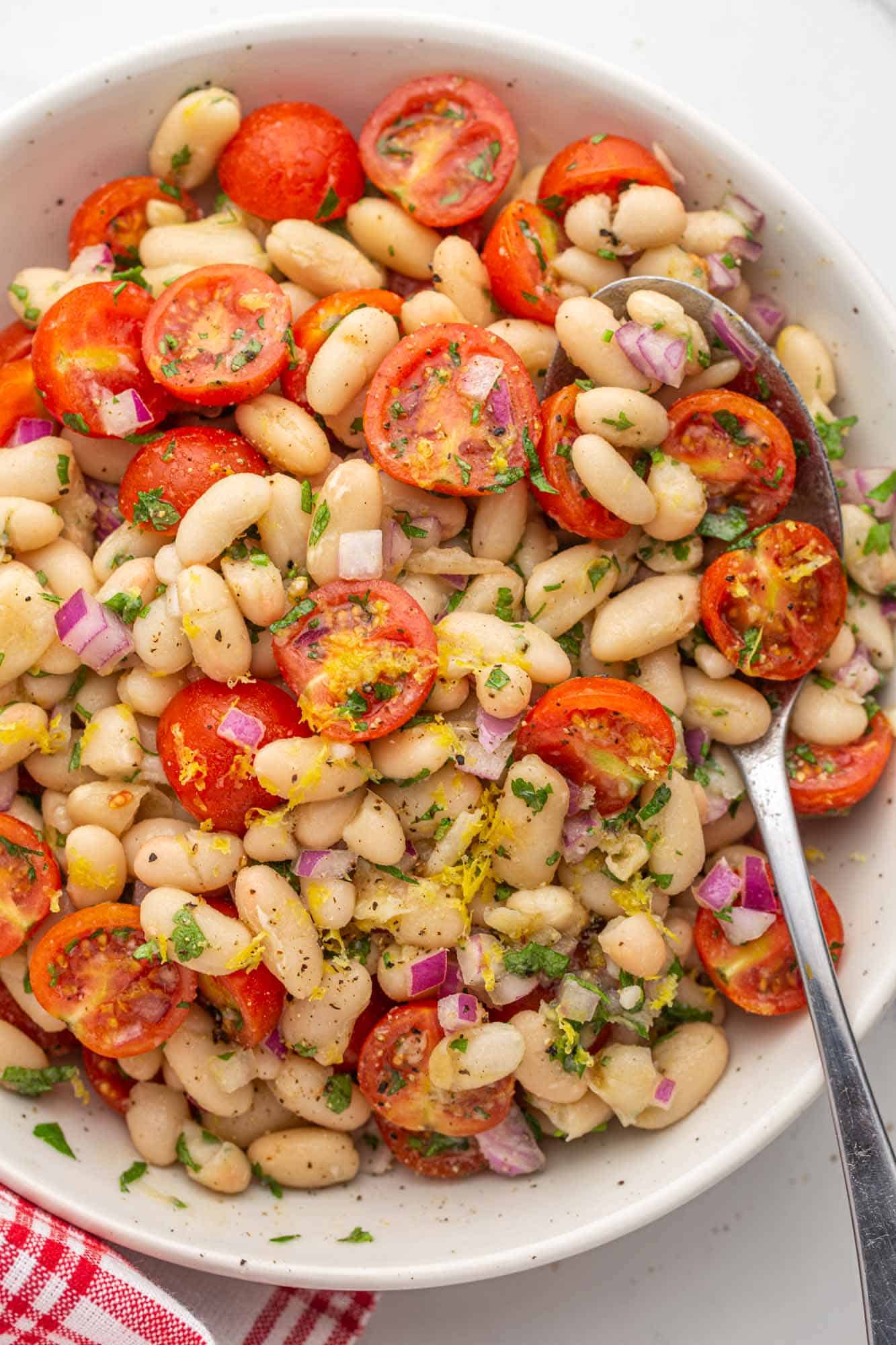 Overhead shot of white bean salad with cherry tomatoes in a white bowl with a serving spoon