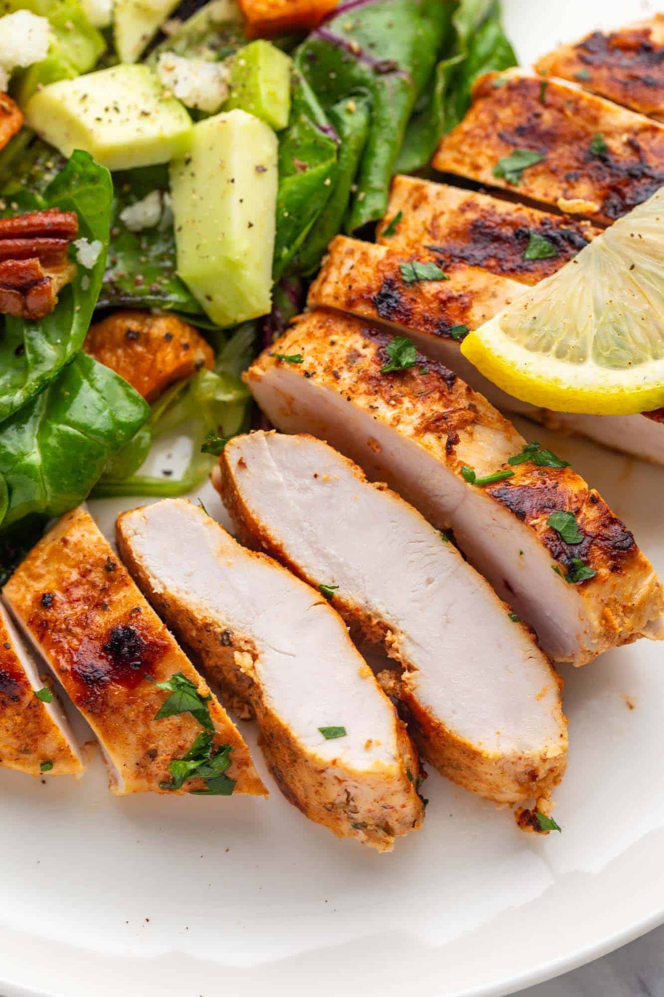Sliced grilled chicken breast served with salad on a white plate