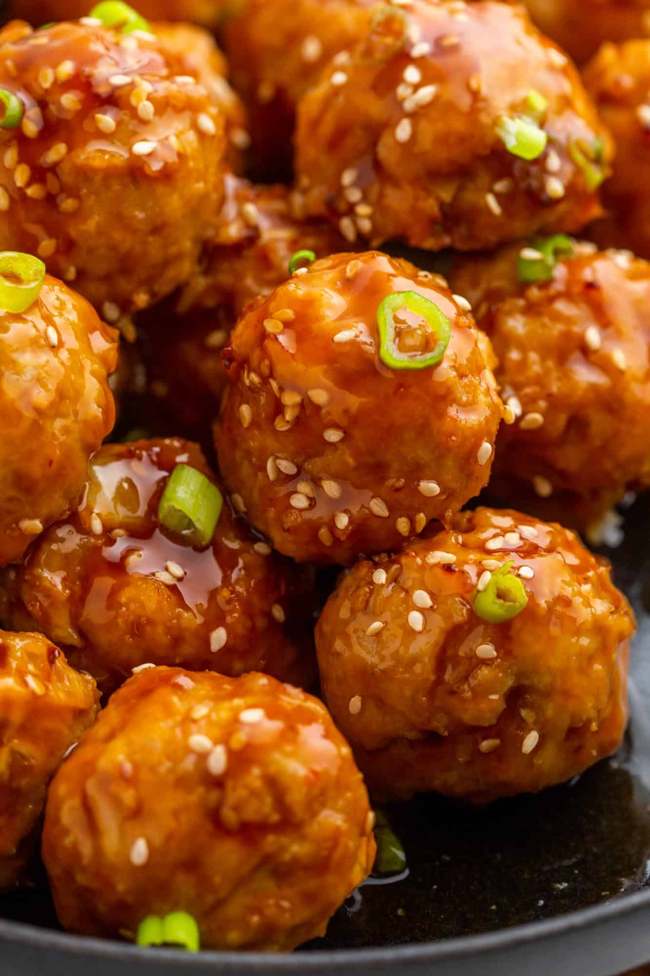 a bowl of chicken meatballs with asian sauce, sliced green onions and sesame seeds