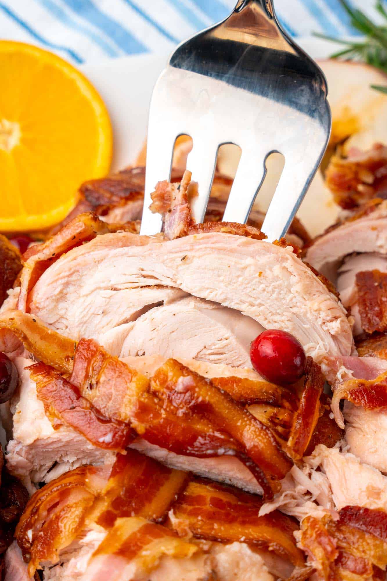 closup view of a sliced bacon wrapped turkey. A serving fork is picking up a slice of white meat.