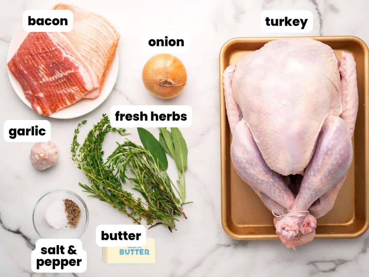 The ingredients needed to make a turkey wrapped in bacon, including a turkey, sliced bacon, onion, garlic, herbs, butter.