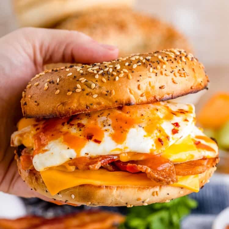 Holding a bagel breakfast sandwich with hot sauce