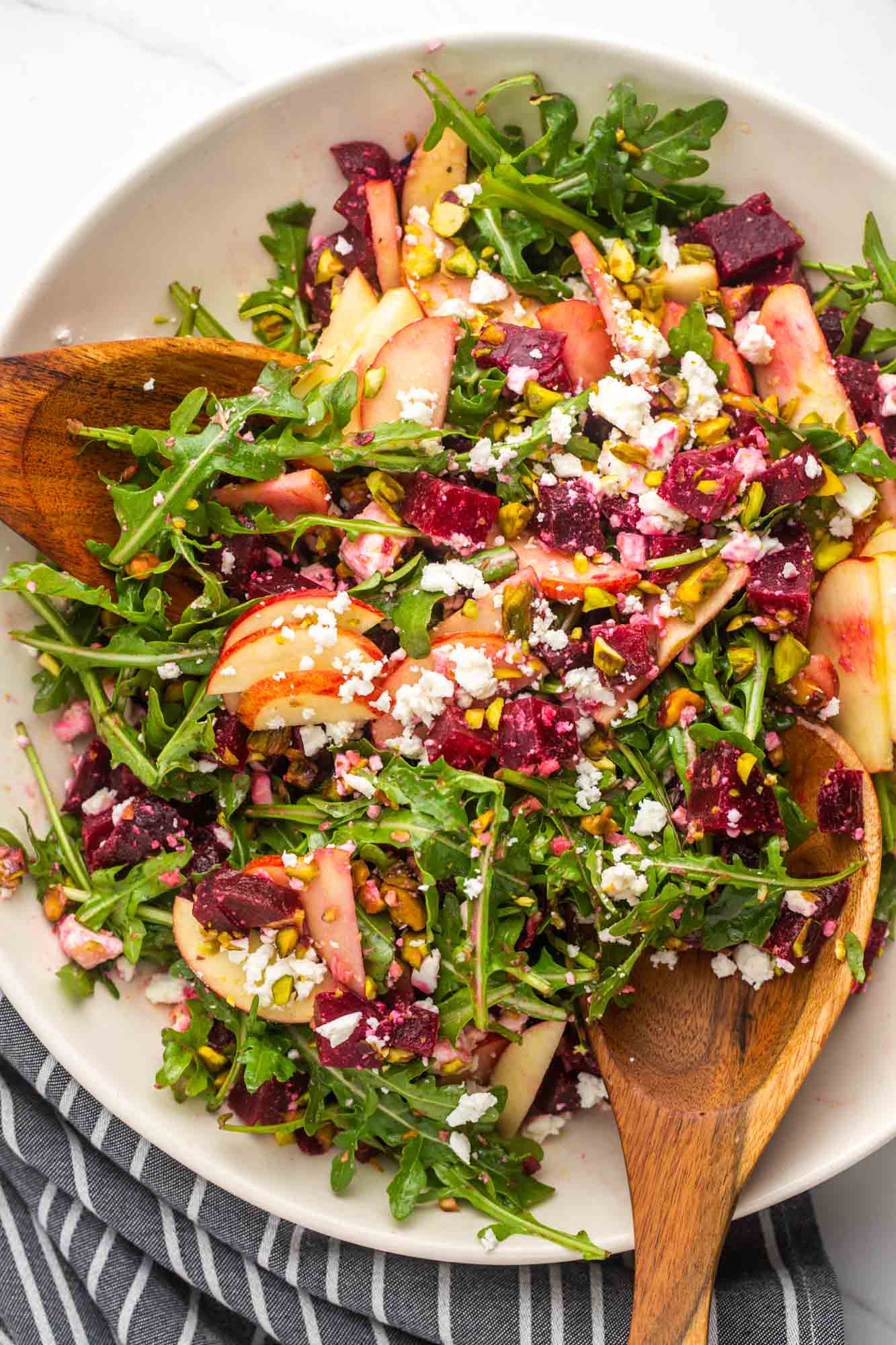 Overhead shot of beet salad in a large white bowl with wooden spoon servers