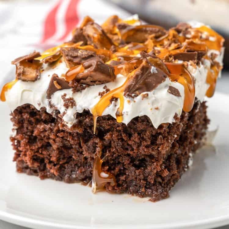 a square slice of bts cake topped with heath bars and caramel, on a white dessert plate.