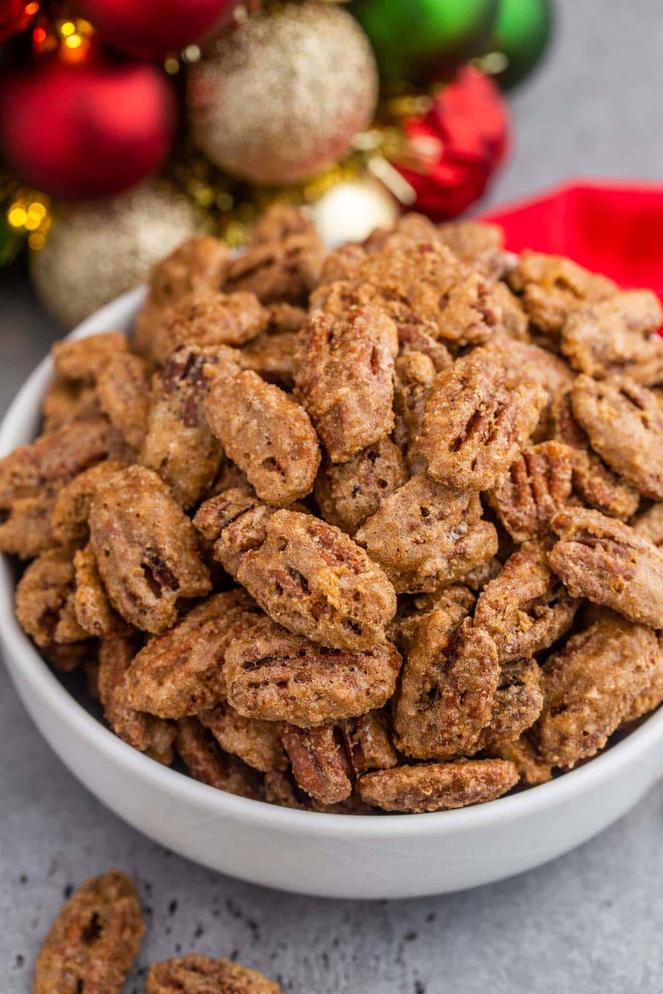 Candied Pecans in a small white bowl, and Christmas decorations in the background.