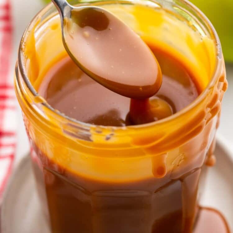 Caramel sauce in a jar with a spoon, and green apples in the background