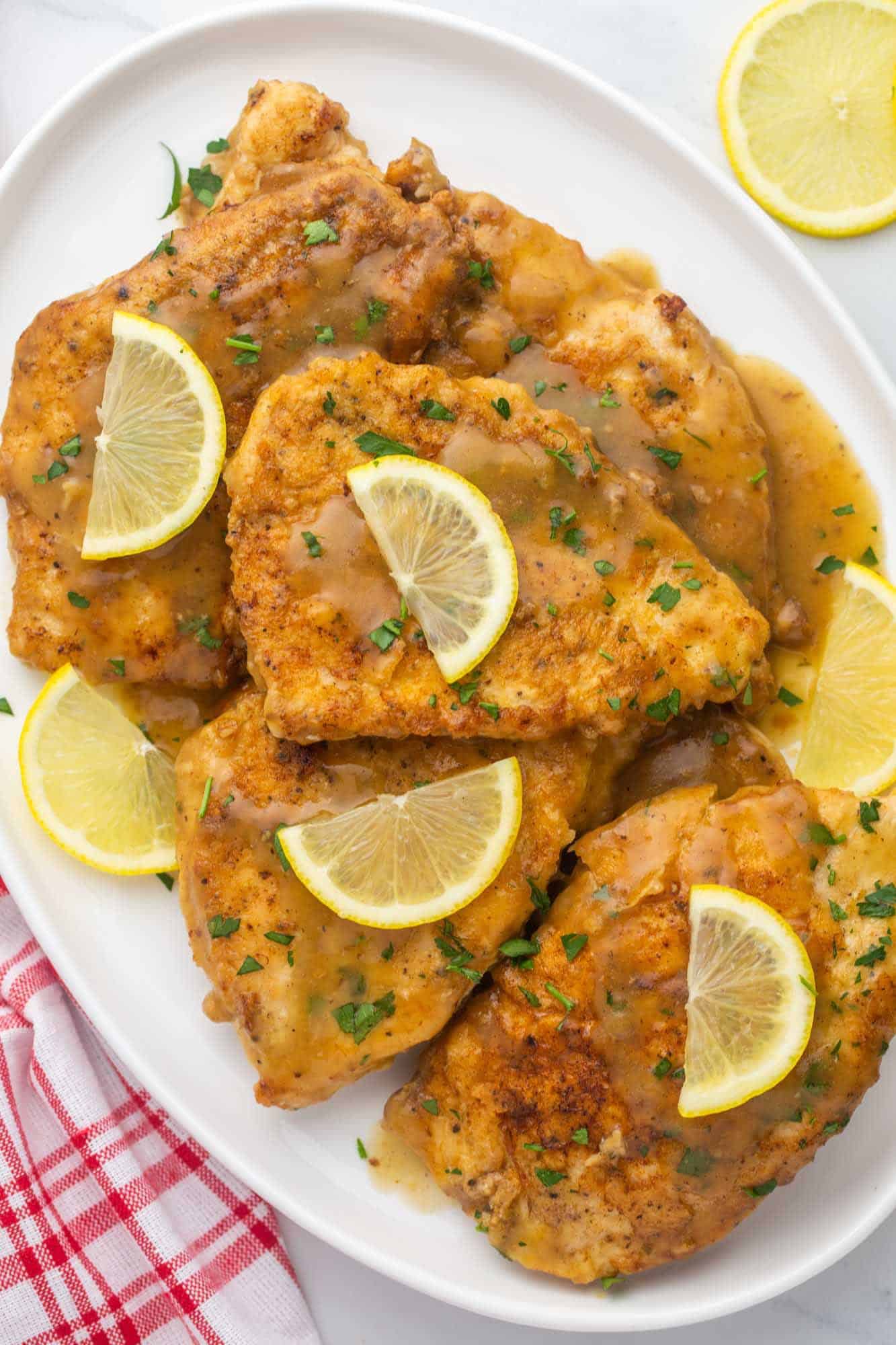 a platter of chicken francese cutlets, topped with thin half slices of lemon. 
