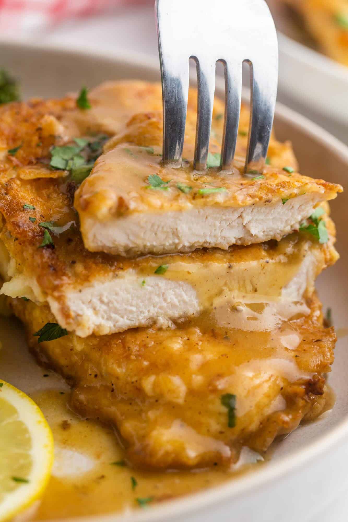 chicken francese on a plate, a piece has been cut in half to show interior texture of the chicken.
