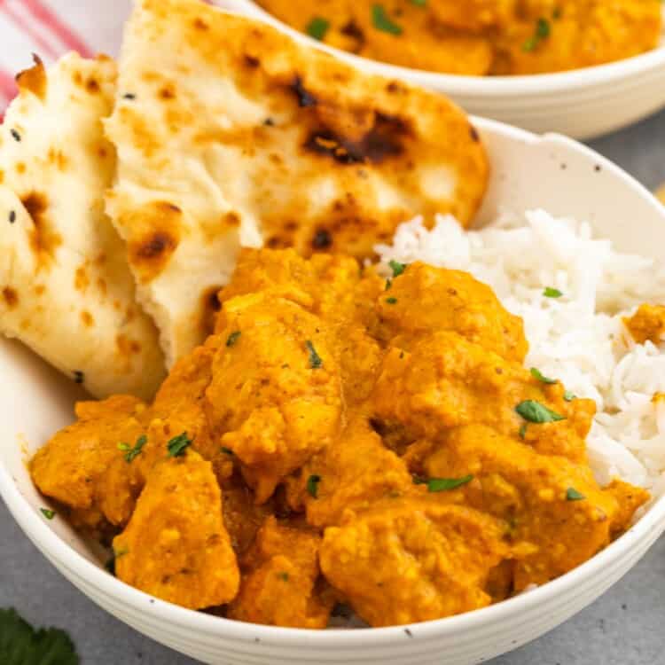 A bowl of chicken korma over rice with torn pita bread on the side.