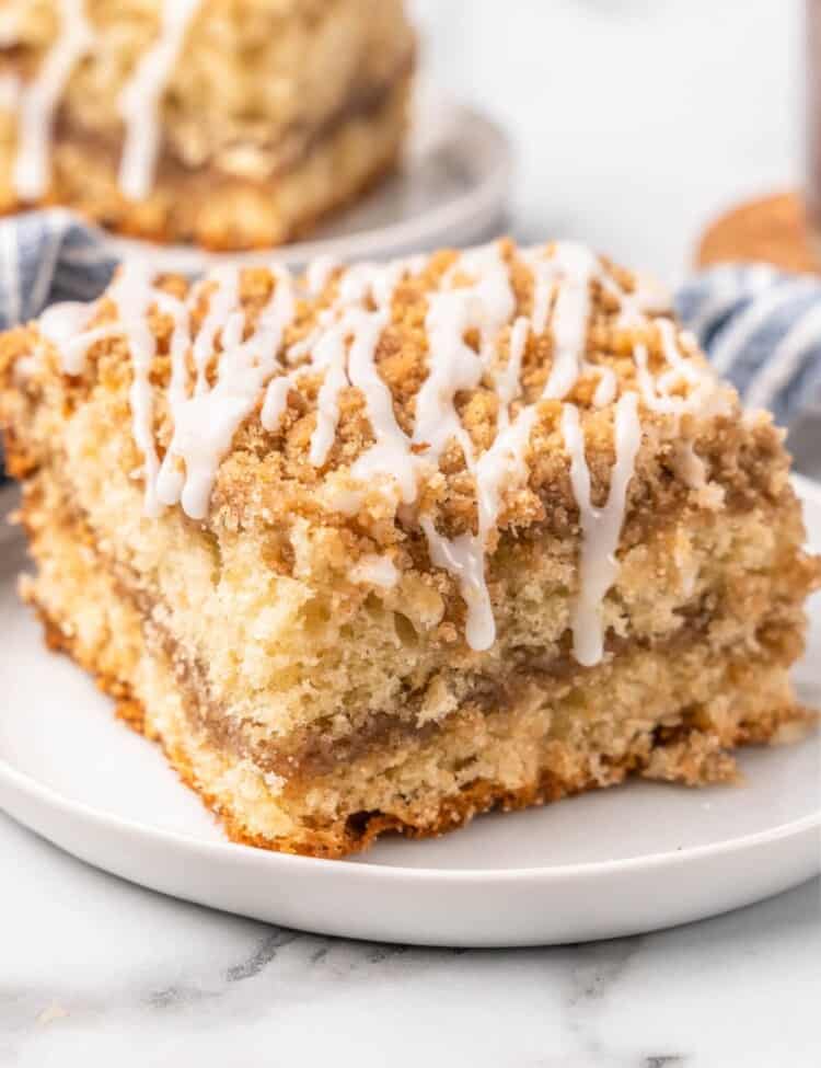 a large square piece of coffee cake, drizzled with glaze, on a white plate.