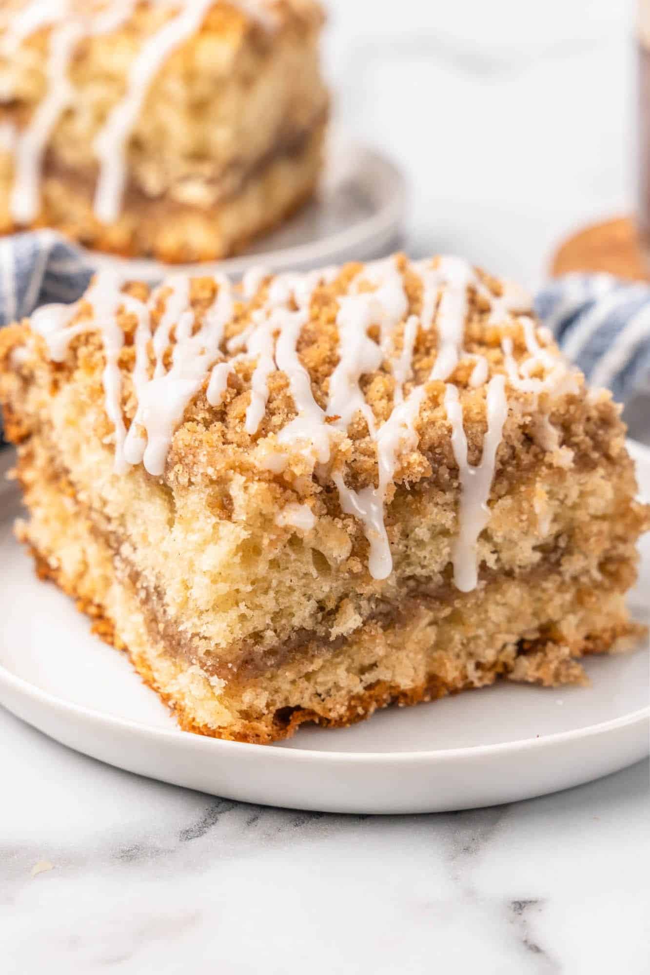 a large square piece of coffee cake, drizzled with glaze, on a white plate. 