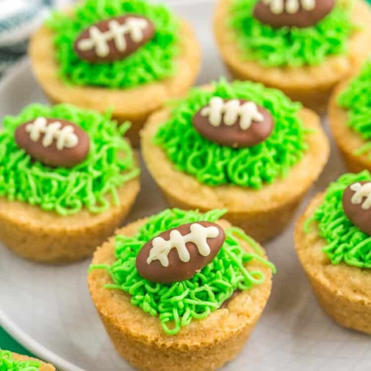 Football cookie cups with chocolate almonds and green buttercream grass, served on a plate that is placed on a green background.
