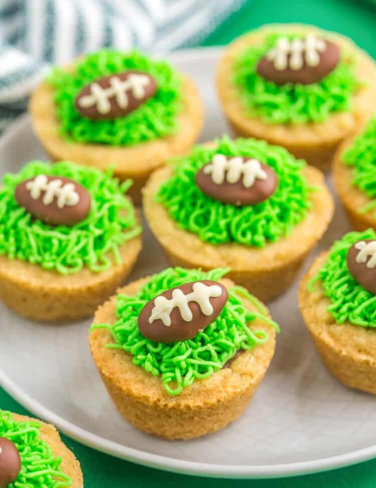 Football cookie cups with chocolate almonds and green buttercream grass, served on a plate that is placed on a green background.