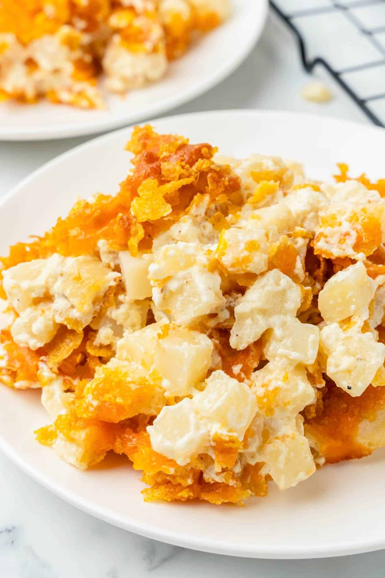 cubed hashbrown potato casserole with cornflake topping. One serving is on a plate. 
