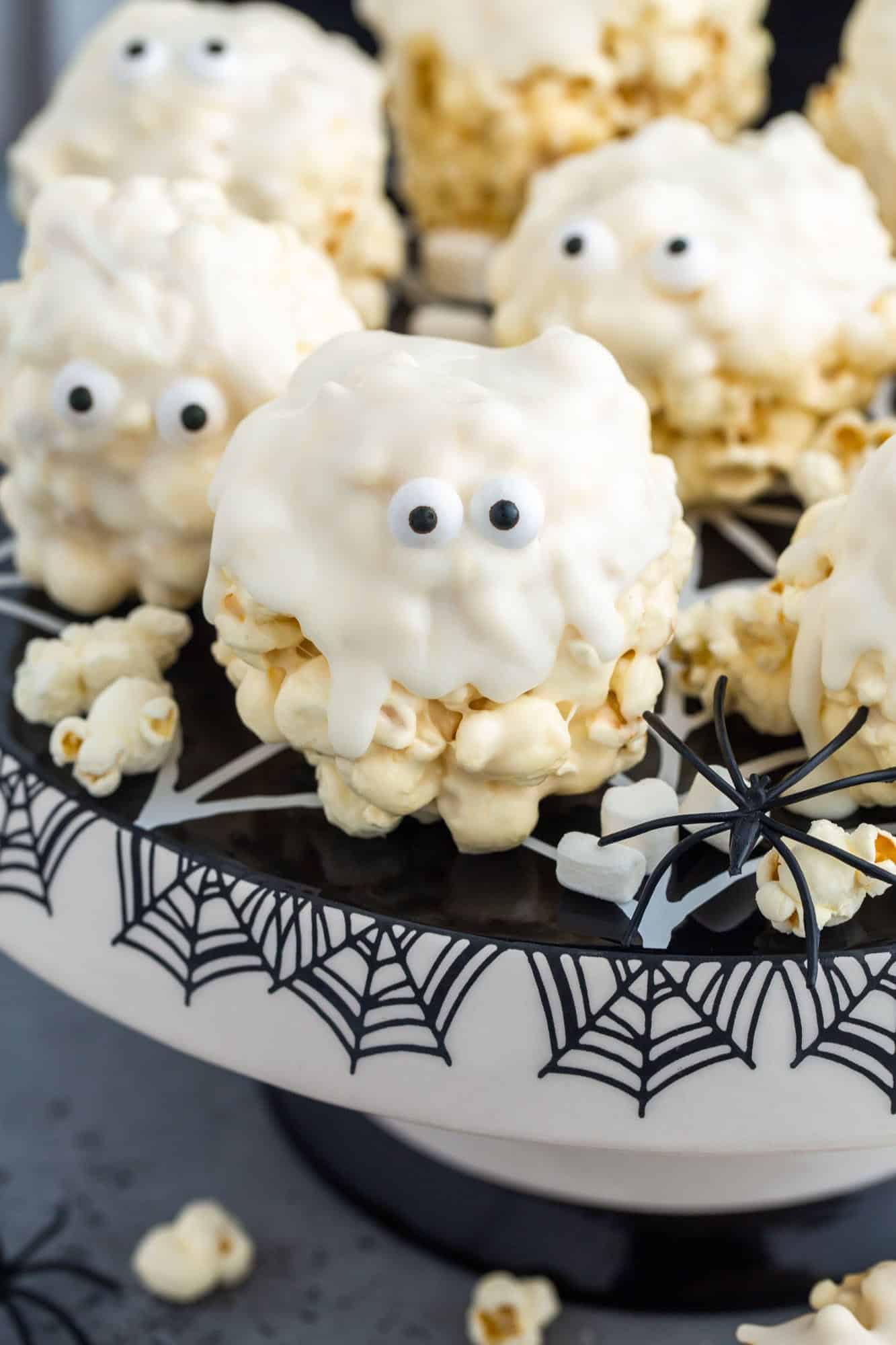 popcorn balls that look like halloween ghosts, on a black and white cake stand decorated with spider webs
