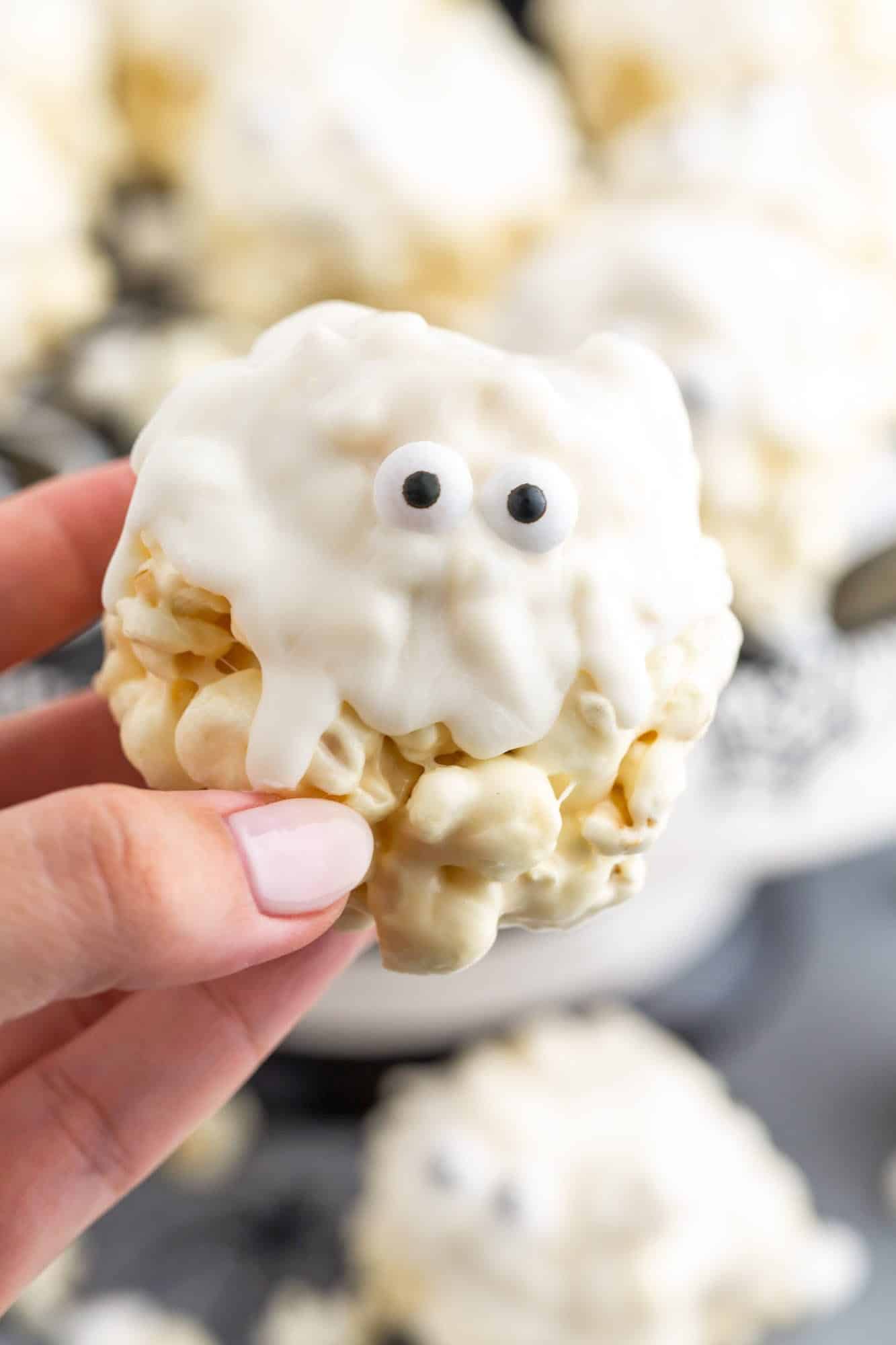 a hand holding a ghost marshmallow popcorn ball with candy eyes