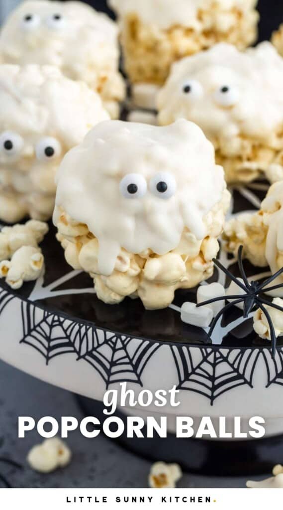 Popcorn balls that are dipped in white chocolate and given candy eyes so that they look cute ghosts. They are on a black and white cake stand decorated with spider webs.