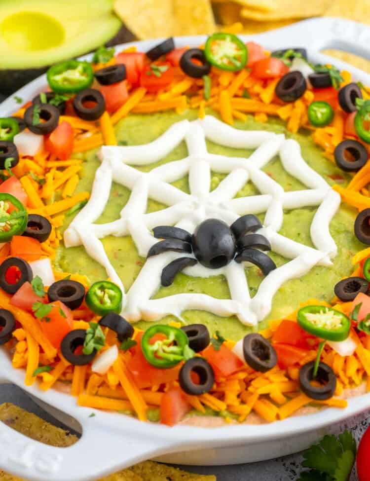 Layered taco dip in a pie plate, decorated with a sour cream spider web for halloween.