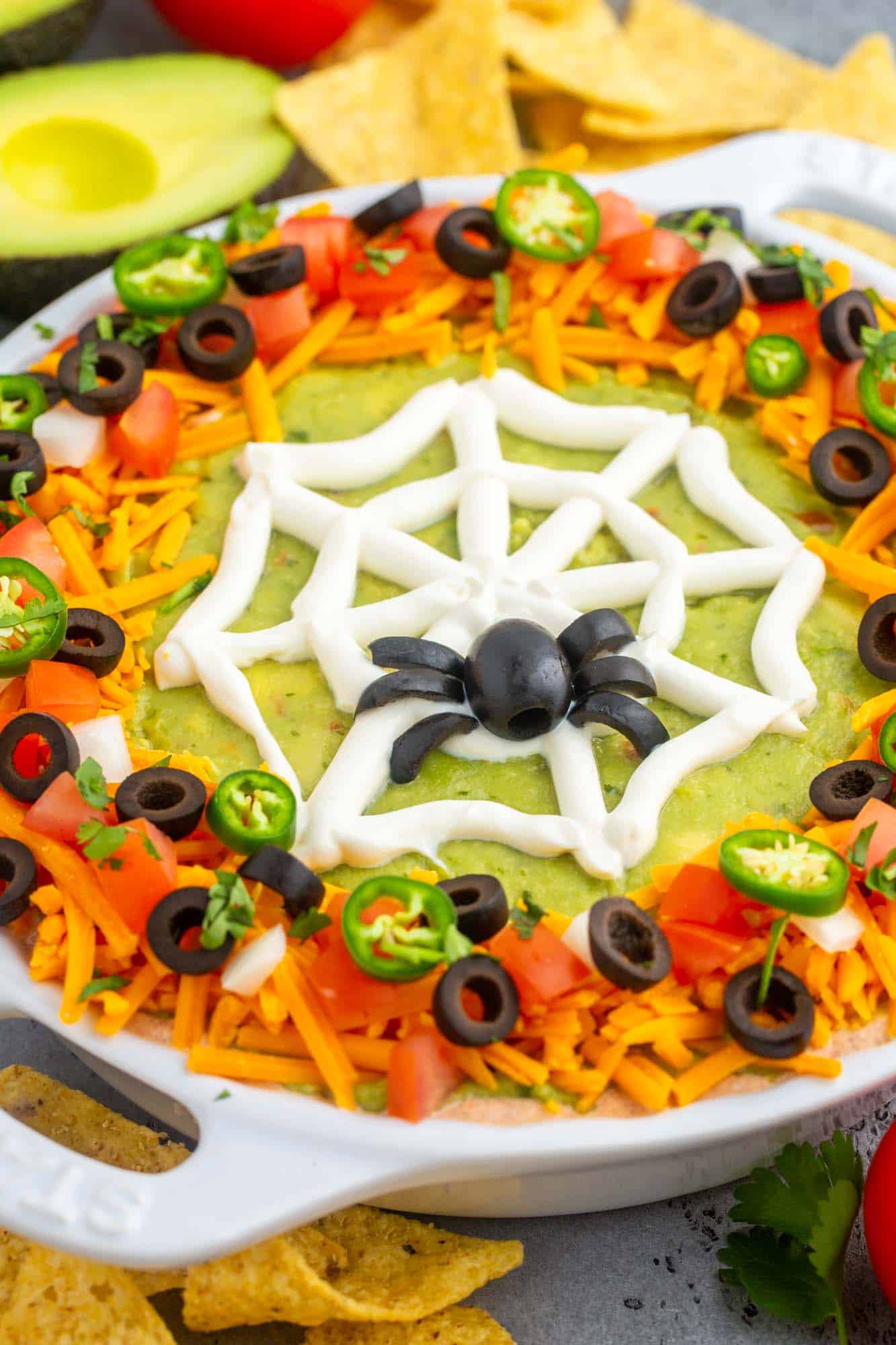 Layered taco dip in a pie plate, decorated with a sour cream spider web for halloween. 