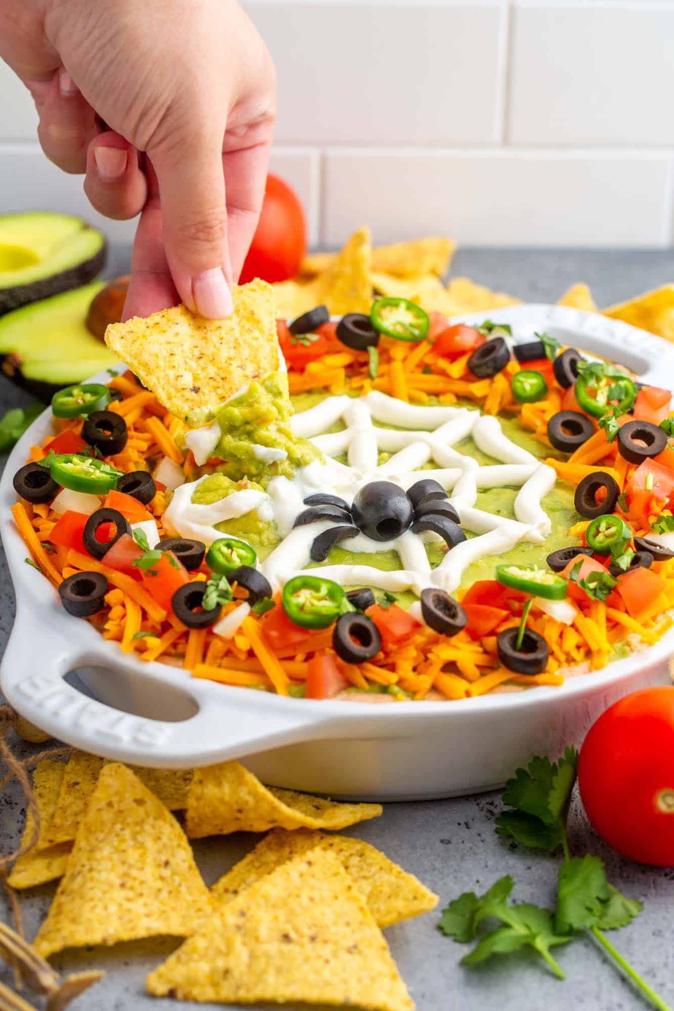 a hand dipping a chip into a halloween taco dip made in a pie plate, with a spider web decoration