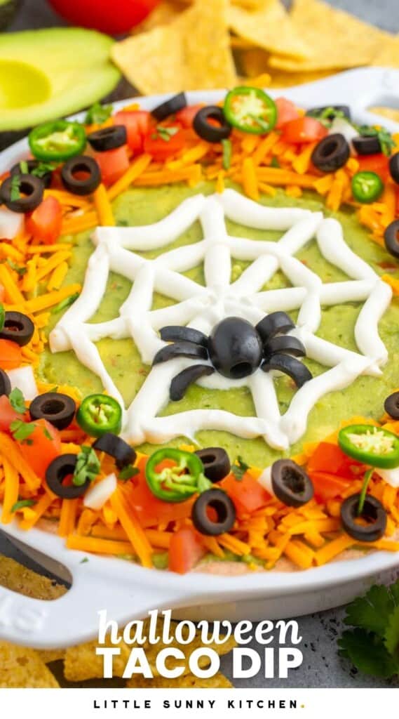 Layered taco dip in a pie plate, decorated with a sour cream spider web for halloween.