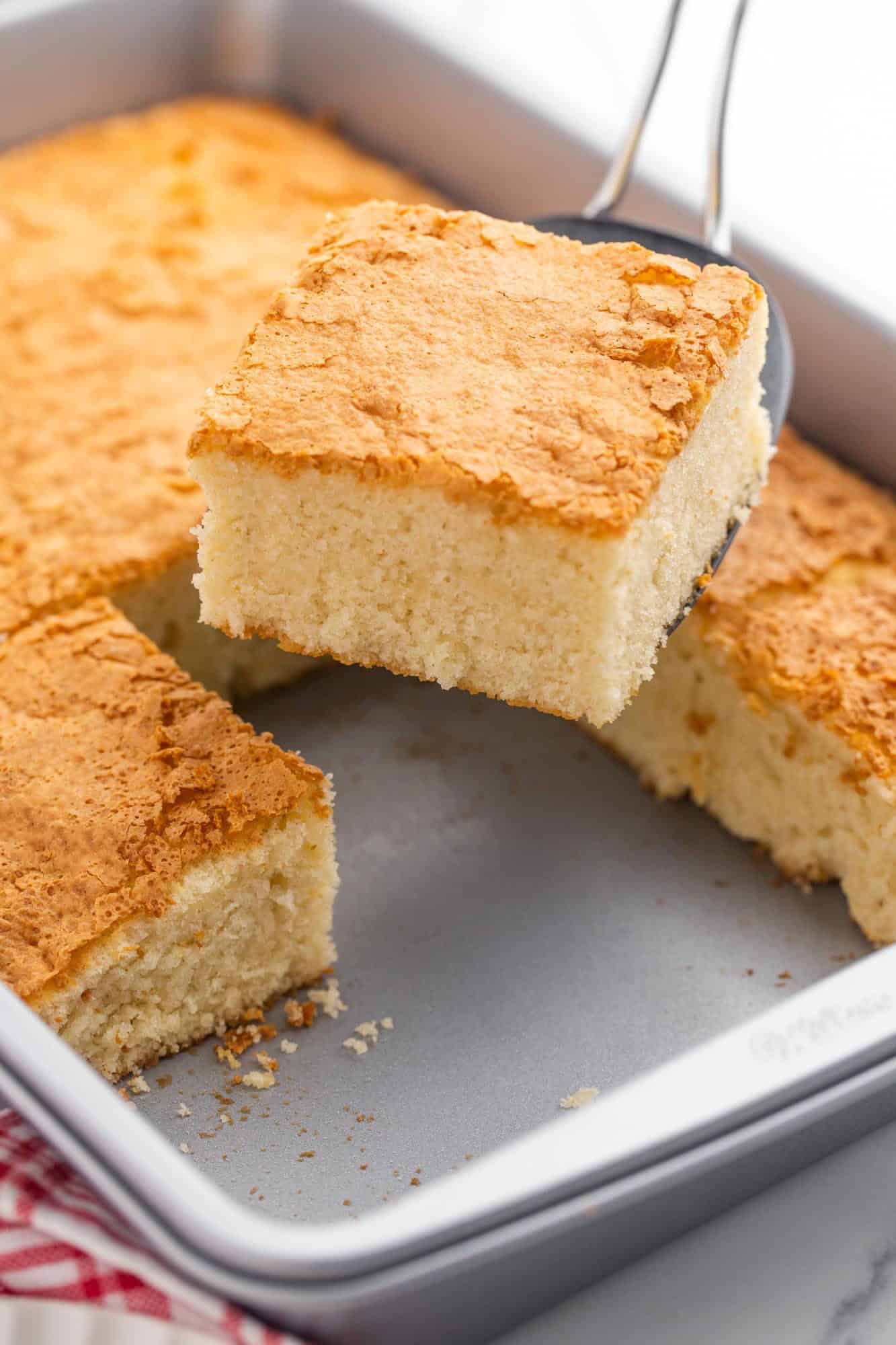 a rectangular cake pan of hot milk cake, cut into squares. A spatula is removing a piece.